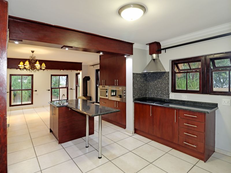 Spacious open-plan kitchen featuring dark wood cabinetry, granite countertops, built-in appliances, and a central island, seamlessly flowing into the adjacent living area.