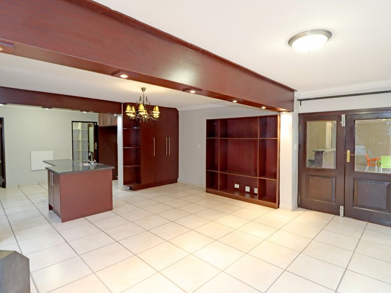 Spacious open-plan living area featuring tiled flooring, built-in wooden cabinetry, a kitchen island with a sink, and a large built-in shelving unit.