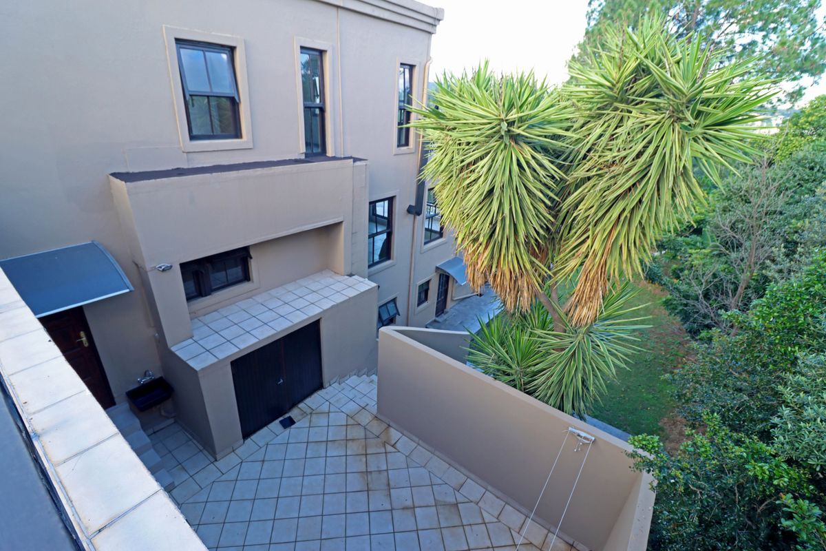 Rear view of a multi-story residential property featuring a tiled patio area, external basin, and landscaped garden surroundings.