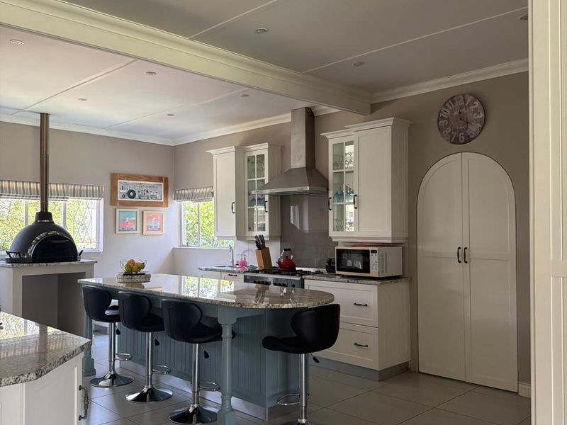 Spacious kitchen featuring a central island with granite countertops, built-in cabinetry, stainless steel extractor fan, and a unique integrated pizza oven.