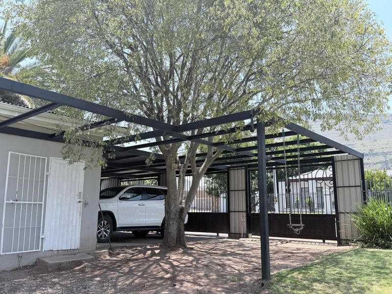A covered carport area featuring a black metal frame structure, providing shaded parking space with integrated security gate access.
