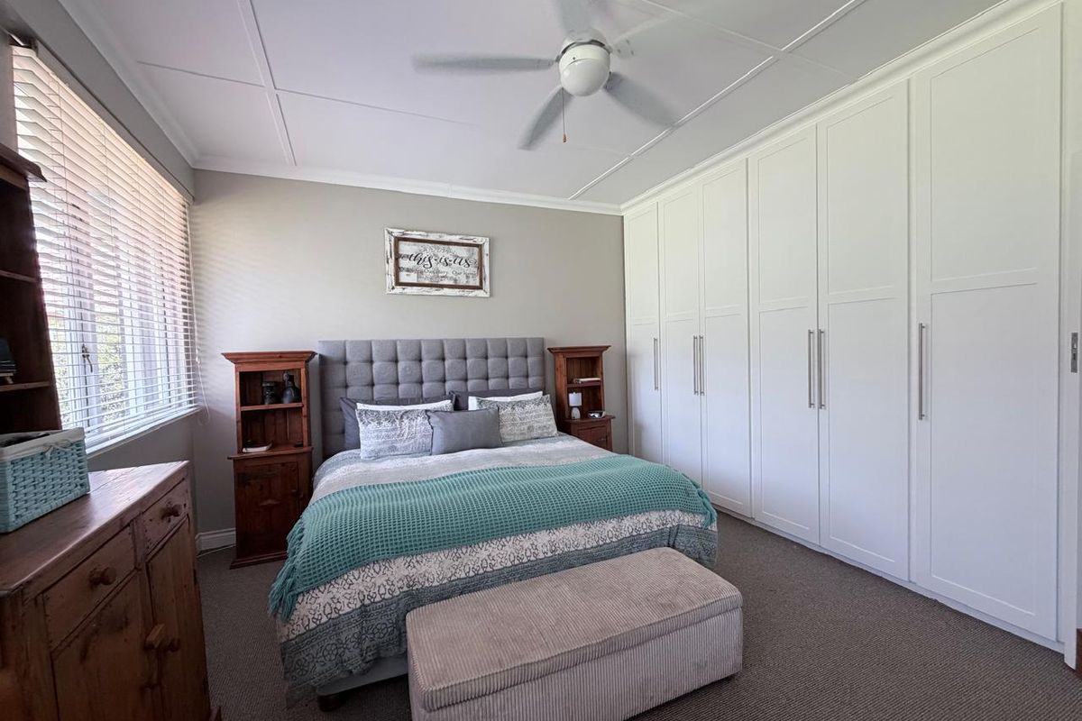A well-maintained bedroom featuring extensive floor-to-ceiling built-in wardrobes, a ceiling fan, and neutral carpeting.