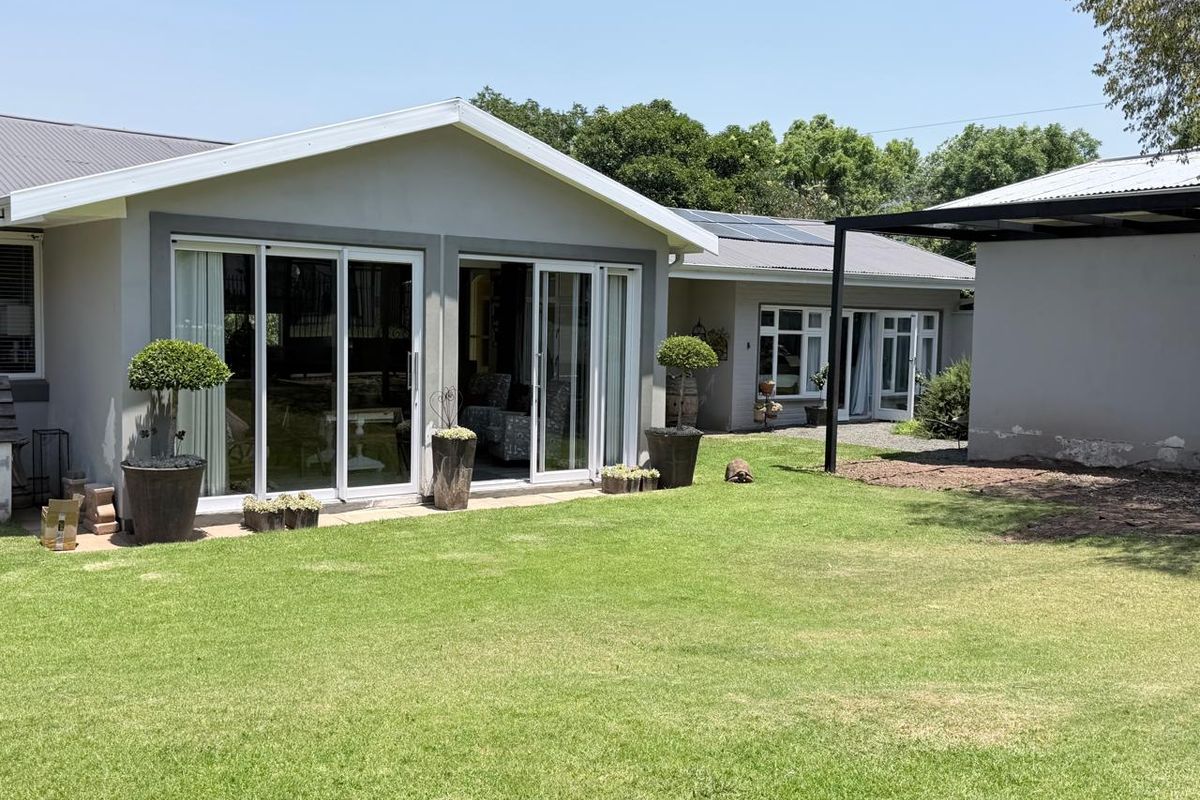 Rear view of the house featuring a well-maintained lawn, sliding glass doors, and a covered patio area with solar panels on the roof.