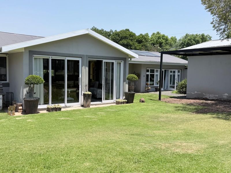 Rear view of the house featuring a well-maintained lawn, sliding glass doors, and a covered patio area with solar panels on the roof.