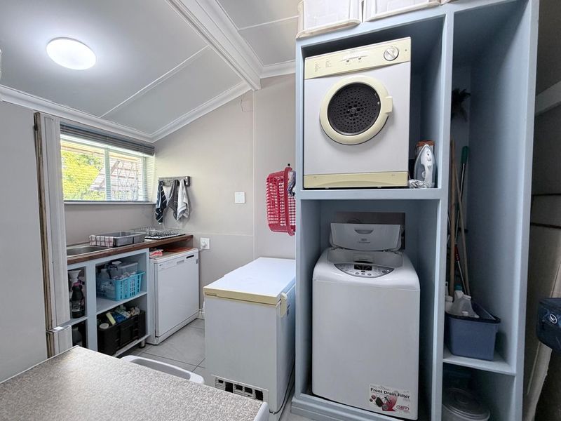 Functional laundry room featuring built-in shelving, a stainless steel sink, and dedicated space for laundry appliances and additional storage.