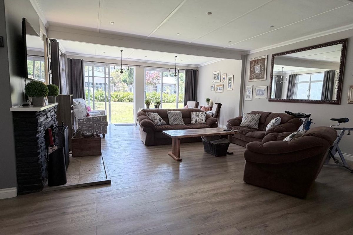 Spacious living room featuring wood-look tile flooring, a stone-clad fireplace, and large sliding glass doors providing direct access to the rear garden.