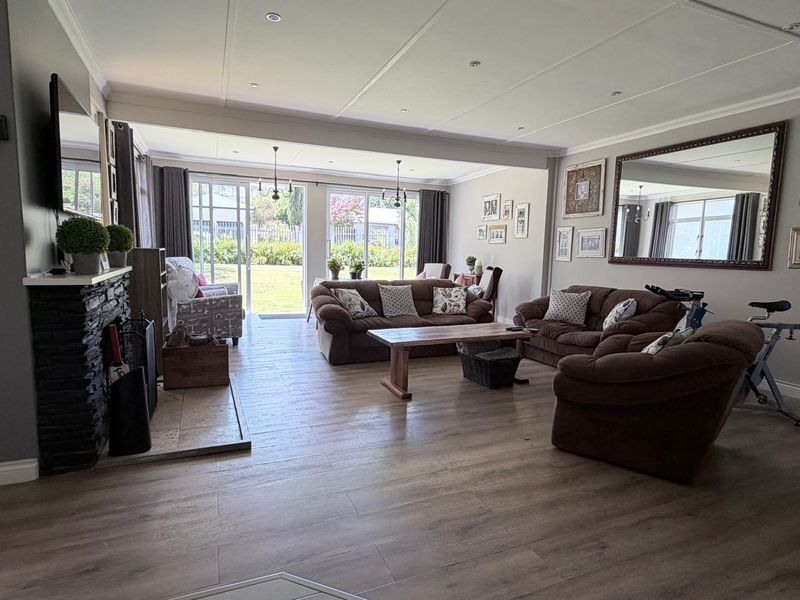 Spacious living room featuring wood-look tile flooring, a stone-clad fireplace, and large sliding glass doors providing direct access to the rear garden.