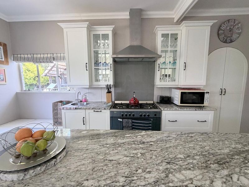 A well-maintained kitchen featuring white cabinetry, granite countertops, a gas stove with a stainless steel extractor fan, and a double-door pantry cupboard.