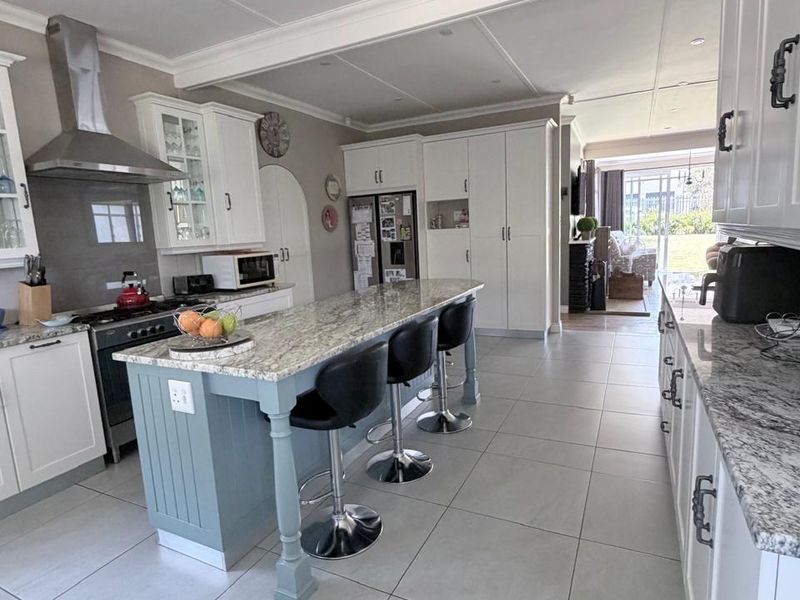 Modern open-plan kitchen featuring a central island with granite countertops, white cabinetry, stainless steel extractor fan, and large format floor tiles.