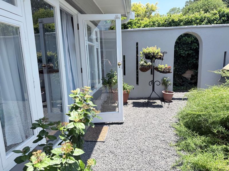 A private rear courtyard featuring a gravel surface, white boundary wall with an arched opening, and direct access to the home via glass doors.