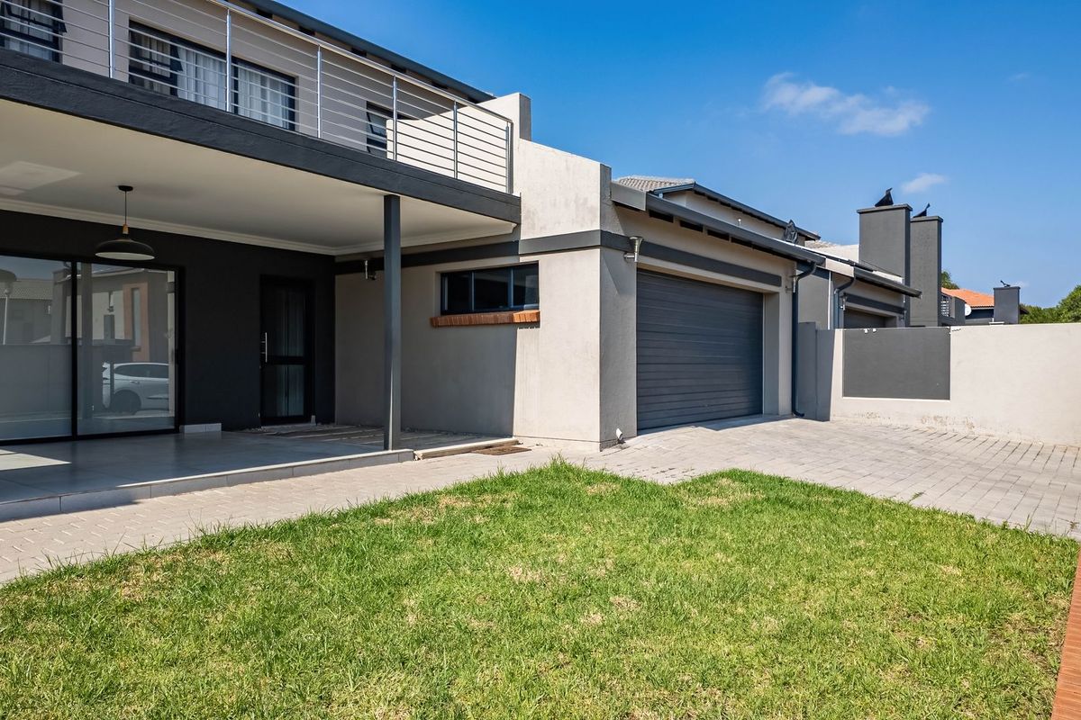 Rear view of the property featuring a covered patio, paved driveway, double garage, and a well-maintained lawn area.