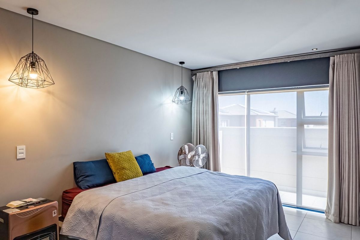 A well-lit bedroom featuring modern pendant lighting, neutral wall finishes, tiled flooring, and large sliding glass doors providing access to an outdoor balcony area.