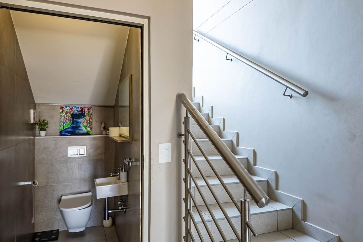 A modern guest bathroom featuring tiled walls and a wall-mounted toilet, situated adjacent to a staircase with stainless steel railings.