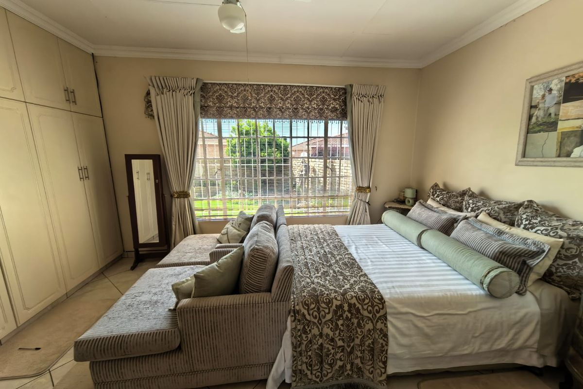A spacious bedroom featuring built-in cupboards, tiled flooring, and a ceiling fan, with large windows fitted with security bars for added peace of mind.