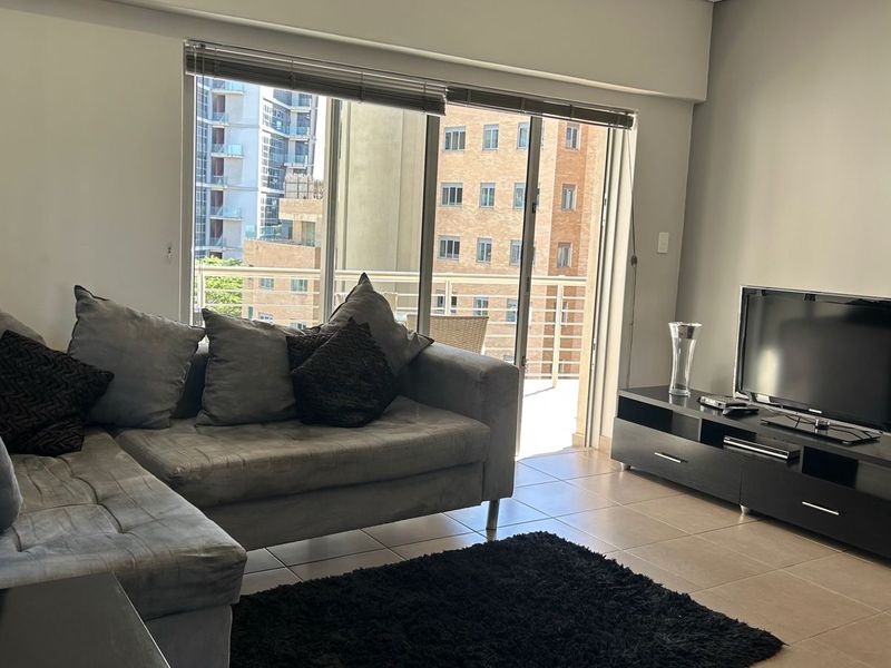 A well-lit living room featuring tiled flooring and a large sliding glass door that opens onto a balcony with urban views.