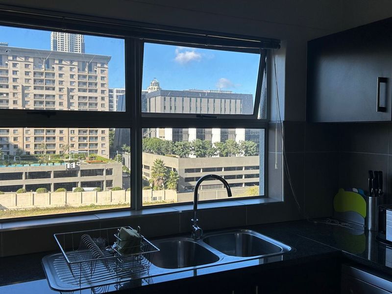 A functional kitchen area featuring dark cabinetry, granite countertops, and a double bowl sink, complemented by large windows offering an urban city view.