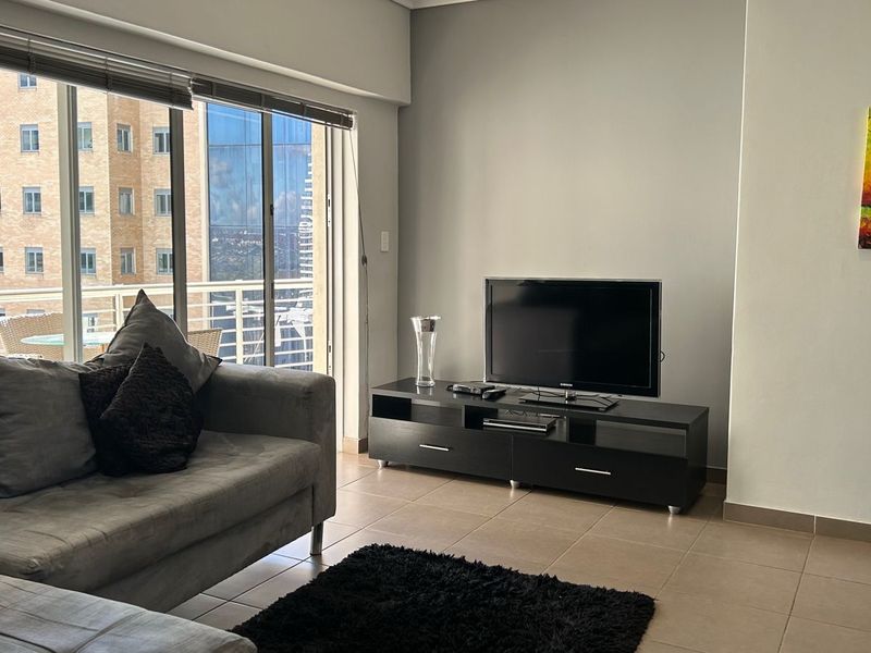 A bright living room featuring large sliding glass doors that open to a balcony, providing natural light and urban views.