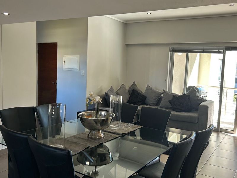 An open-plan living and dining area featuring neutral tiled flooring, recessed lighting, and direct access to a balcony through large sliding glass doors.