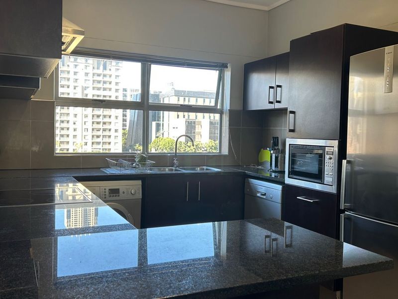 Modern kitchen featuring dark wood cabinetry, granite countertops, tiled backsplash, and integrated appliances, offering a functional and sleek workspace with city views.
