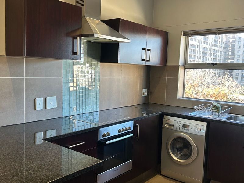 A functional kitchen featuring dark wood cabinetry, granite countertops, a built-in oven with hob, and a stainless steel extractor fan.