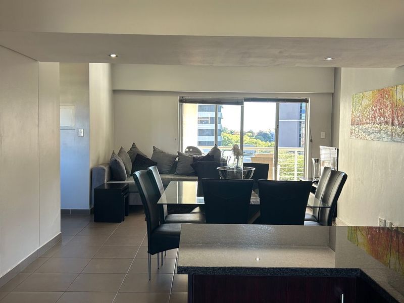 Open-plan living and dining area featuring tiled floors, recessed lighting, and a sliding glass door leading to a balcony.