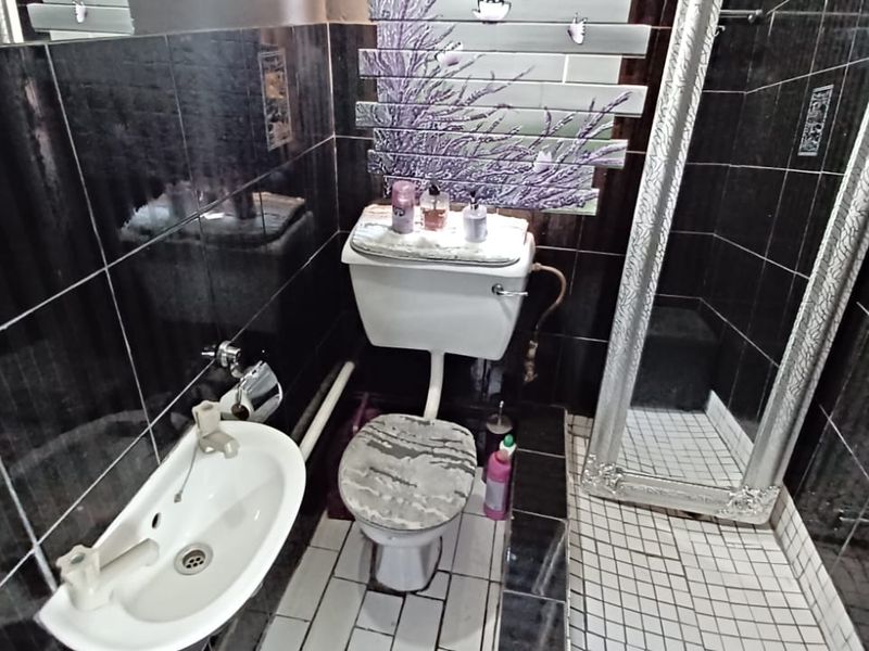 Compact bathroom featuring dark wall tiles, a wall-mounted basin, toilet, and a shower enclosure with visible plumbing.