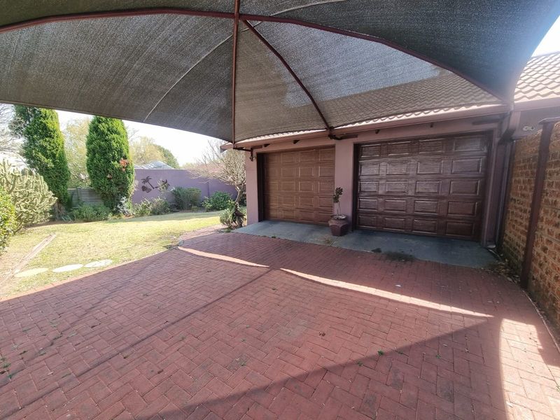 Double garage with a shade cloth carport and brick paved driveway, set within a private garden area.