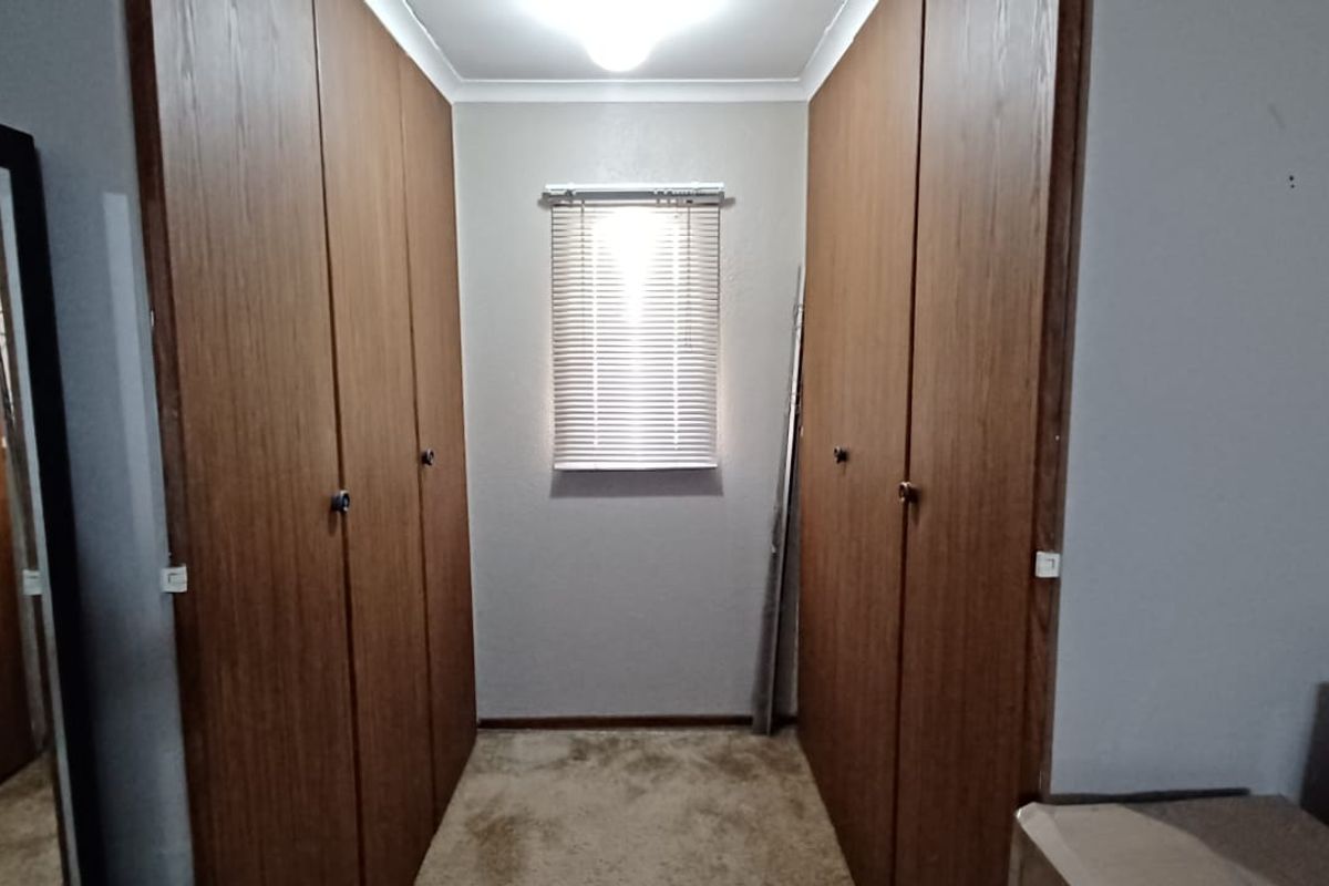 A bedroom featuring extensive built-in wooden cupboards, carpeted flooring, and a window fitted with venetian blinds.