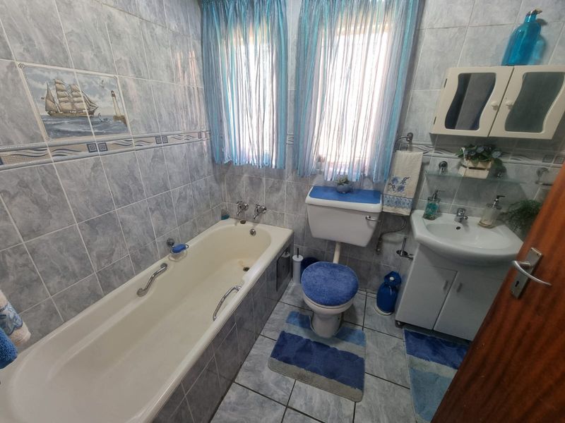 A functional bathroom featuring a bathtub, toilet, and vanity basin with full-height wall tiling and tiled flooring.