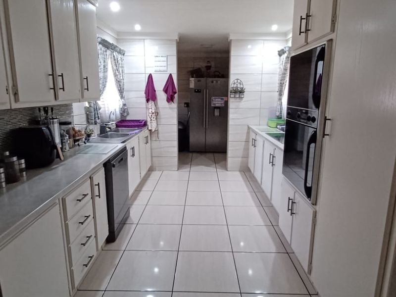 A functional galley-style kitchen featuring white cabinetry, double wall ovens, tiled backsplash, and tiled flooring with ample counter space.