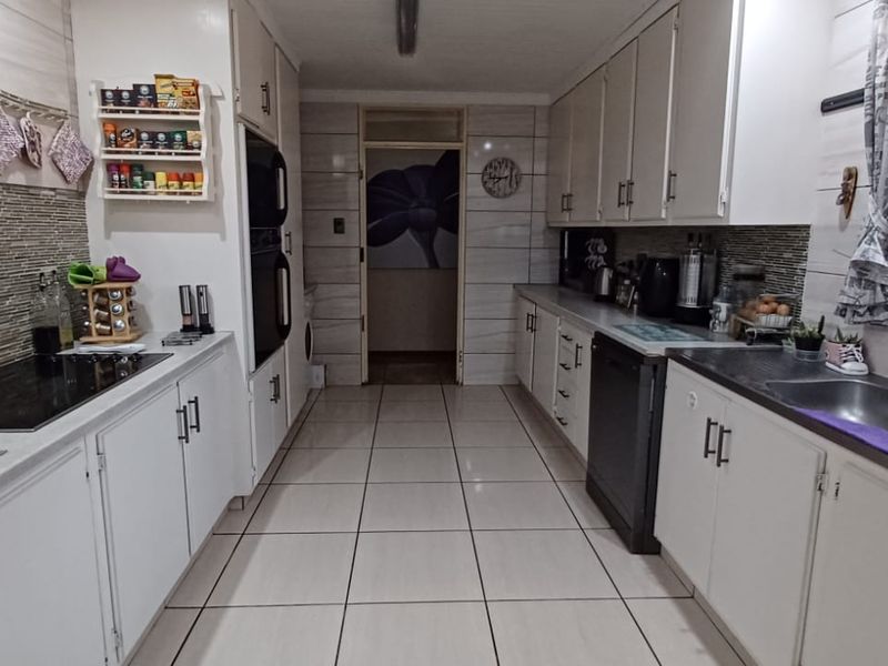 A functional galley-style kitchen featuring white cabinetry, tiled flooring, a built-in oven, electric hob, and a double sink with tiled backsplash.