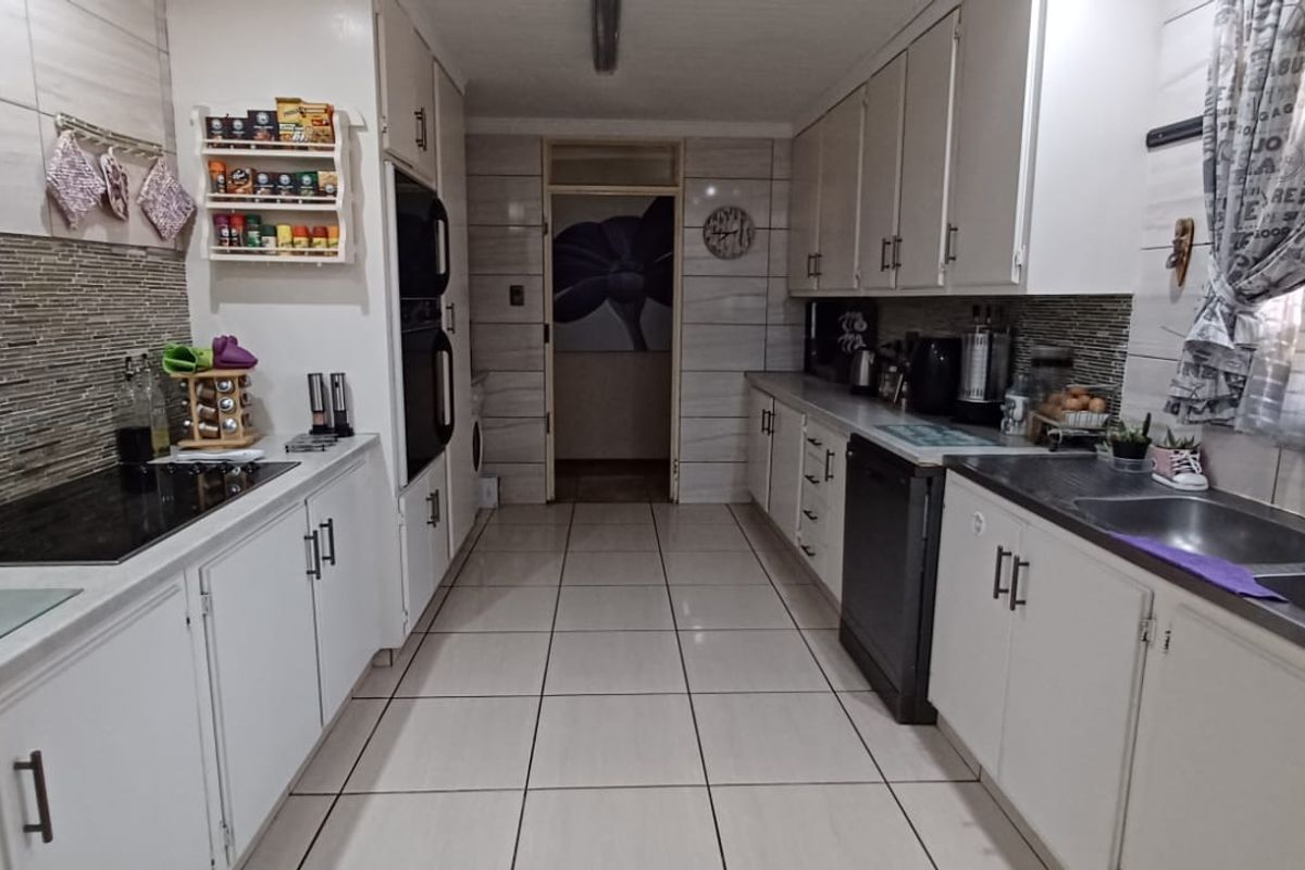A functional galley-style kitchen featuring white cabinetry, tiled flooring, a built-in oven, electric hob, and a double sink with tiled backsplash.
