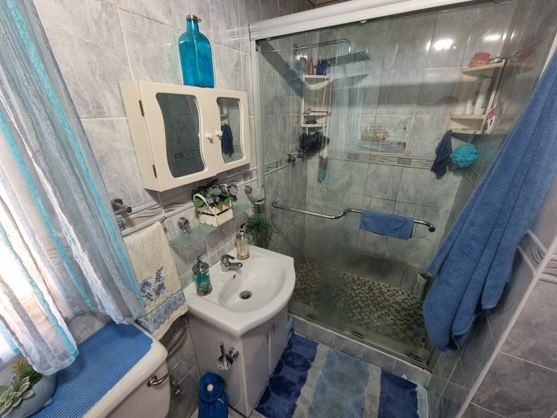 Compact bathroom featuring a tiled shower enclosure with glass door, vanity basin with storage cabinet, and wall-mounted medicine cabinet.