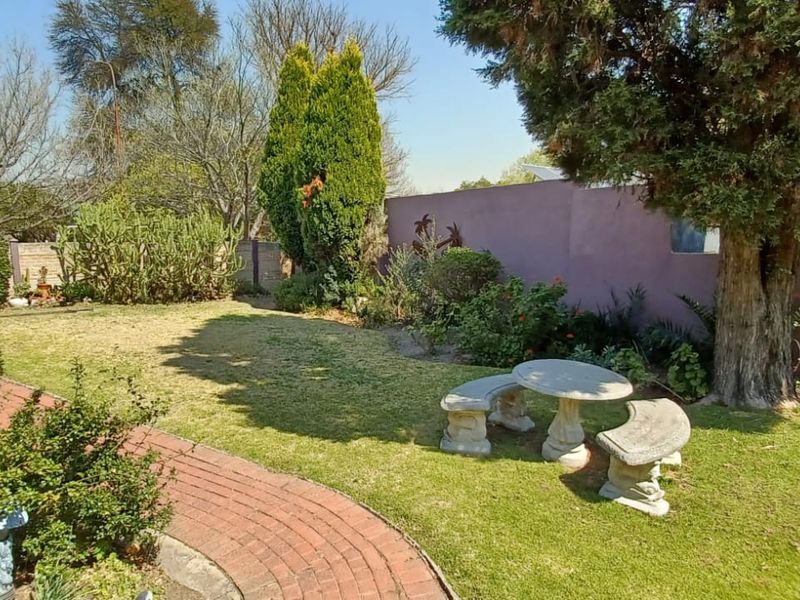 A well-maintained residential garden featuring a brick paved pathway, mature trees, and established landscaping enclosed by a boundary wall.