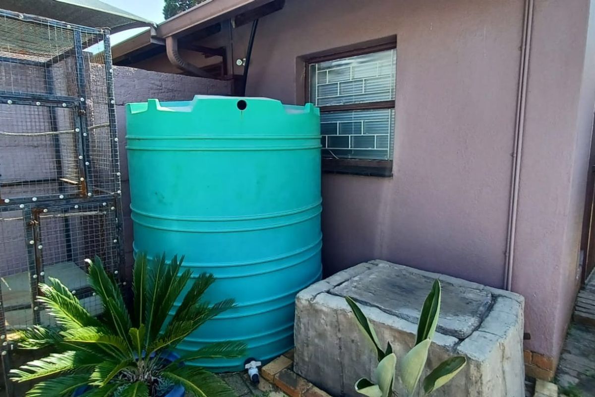 Rear exterior area featuring a large water storage tank on a concrete plinth, adjacent to the main building structure with security-barred window.