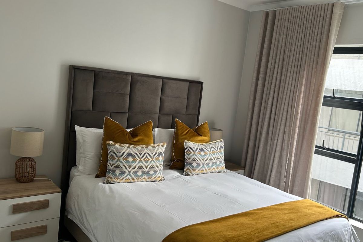 A well-maintained bedroom featuring a large window with floor-to-ceiling curtains, providing ample natural light and a clean, neutral aesthetic.