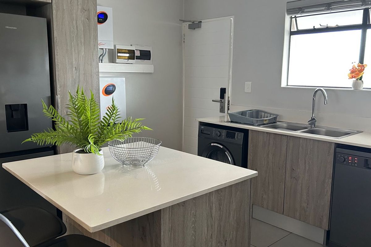 Modern kitchen featuring quartz countertops, wood-look cabinetry, integrated dishwasher, and a dedicated wall-mounted inverter system for energy efficiency.