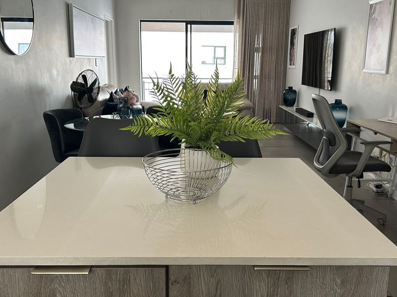 Modern open-plan living area featuring a central kitchen island with stone countertop, tiled floors, and seamless access to a private balcony through sliding doors.