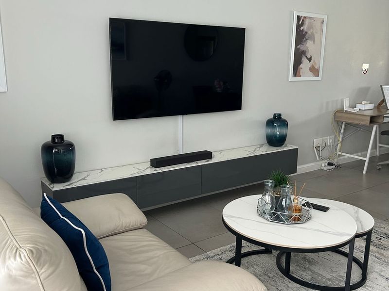 A modern living room featuring a wall-mounted television, a sleek floating media console with a marble-effect top, and neutral tiled flooring.