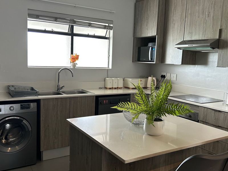 Modern kitchen featuring wood-grain cabinetry, stone countertops, a central island, and integrated appliances including an oven, hob, and extractor fan.