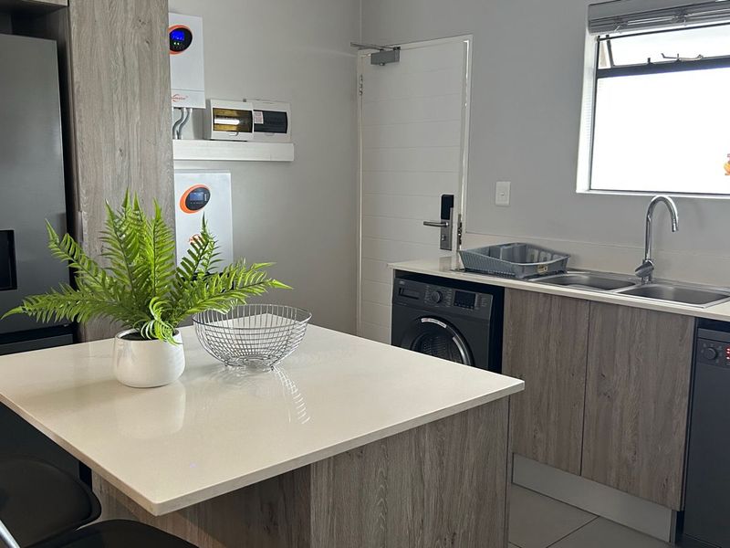 Modern kitchen featuring quartz countertops, wood-look cabinetry, integrated dishwasher, and a dedicated wall-mounted inverter system for energy efficiency.