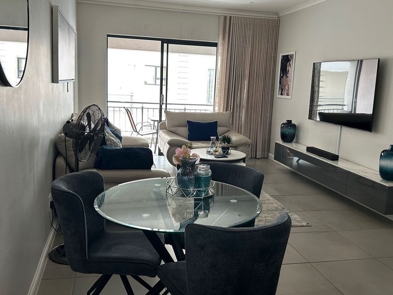 An open-plan living and dining area featuring tiled floors, recessed lighting, and a wall-mounted media console, with direct access to a balcony.