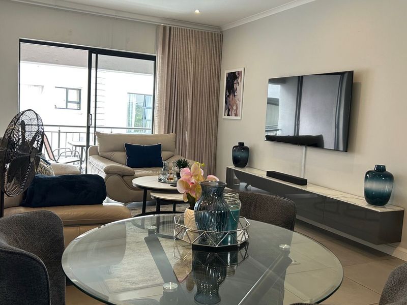 A well-maintained living room featuring tiled floors, recessed lighting, a wall-mounted television, and a floating media console, with access to a balcony.