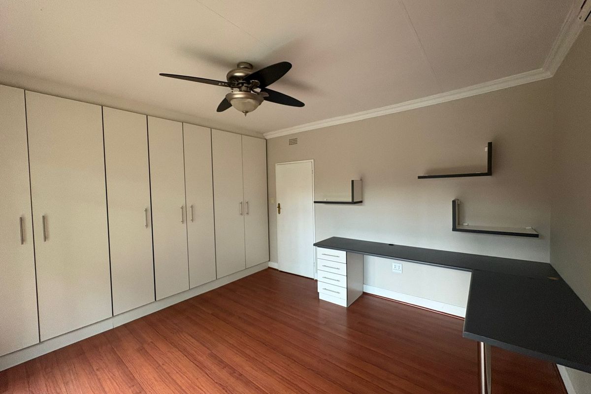 A bedroom featuring extensive built-in cabinetry, a ceiling fan, and a built-in desk with floating shelving.