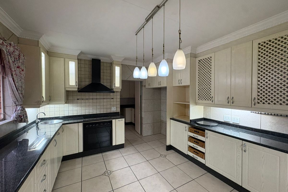 A functional kitchen featuring granite countertops, built-in oven with extractor fan, ample cabinetry, and tiled flooring with a neutral aesthetic.