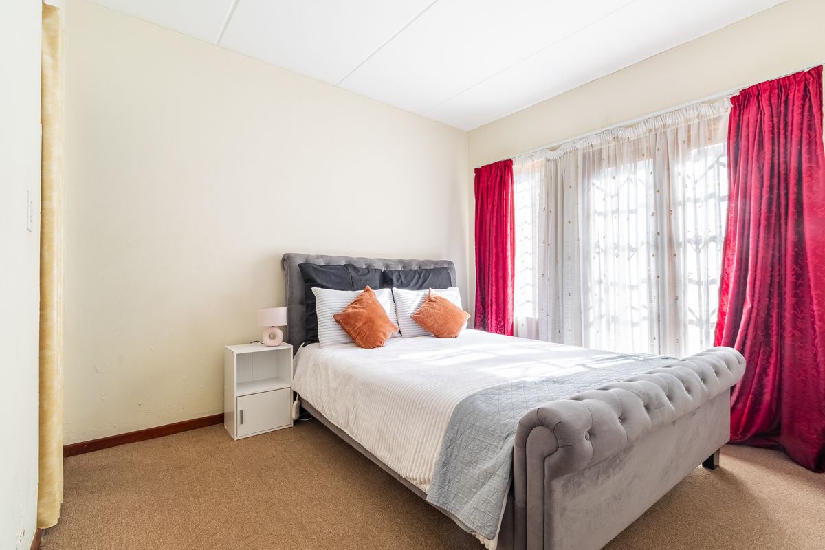 A well-lit bedroom featuring carpeted flooring and a sliding glass door with security gate access, providing natural light and ventilation.