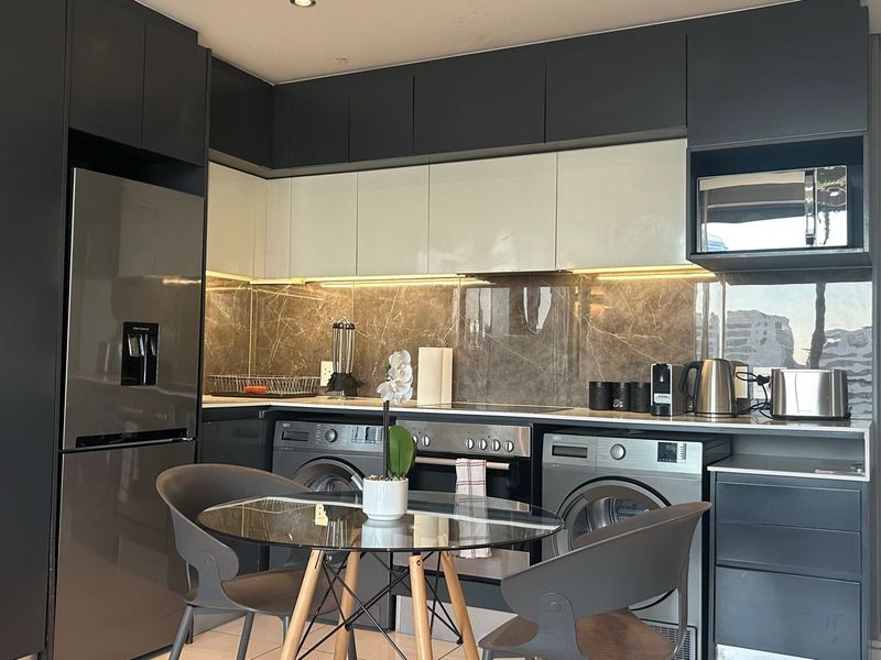 Modern kitchen featuring sleek dark and white cabinetry, stone splashback, integrated appliances, and recessed lighting, offering a contemporary and functional cooking space.