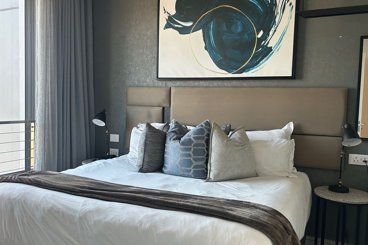 A well-appointed bedroom featuring a large upholstered headboard, neutral wall finishes, and access to a private balcony through sliding glass doors.