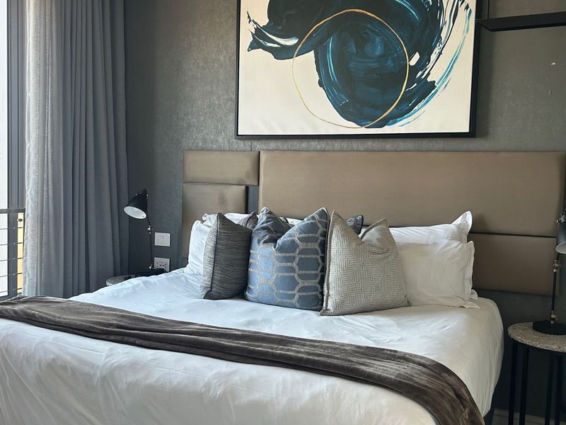 A well-appointed bedroom featuring a large upholstered headboard, neutral wall finishes, and access to a private balcony through sliding glass doors.