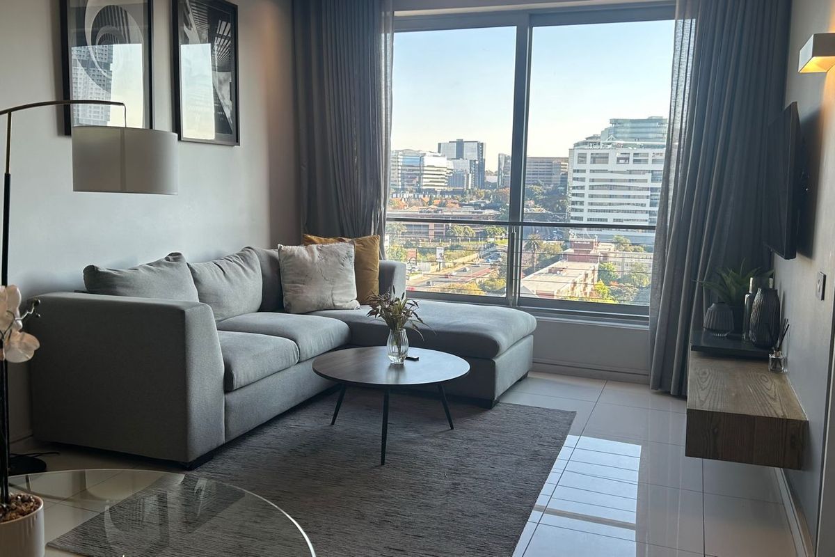 A modern living room featuring large floor-to-ceiling windows with city views, a floating media shelf, and neutral tiled flooring.